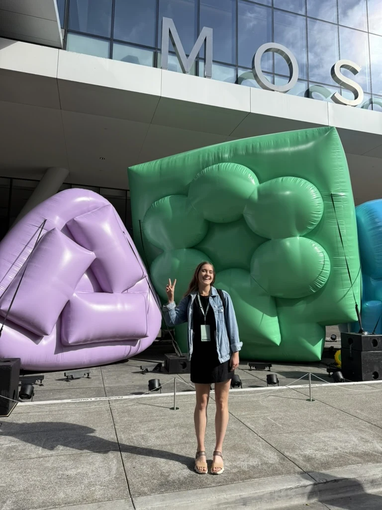 McKenna smiling and holding up a peace sign in front of giant inflatable sculptures at a design conference