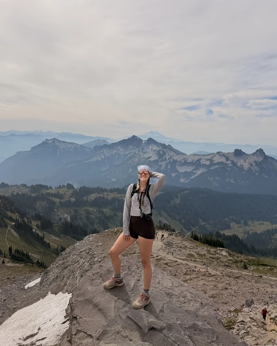 McKenna smiling on a rocky ridge on a hike, with mountain peaks behind her